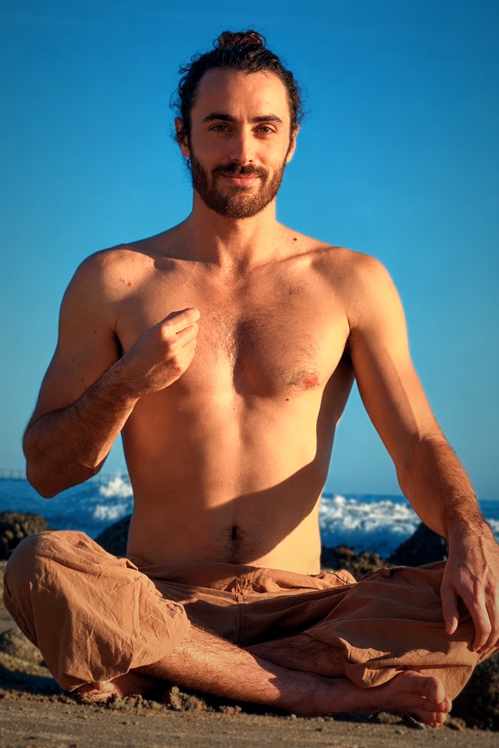 Noah sitting cross-legged on the beach, smiling